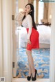 A woman in a red skirt and white shirt posing in a hotel room.