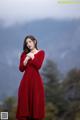 A woman in a red dress standing in front of a mountain.