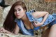 A woman in a blue top and denim shorts laying on a hay bale.