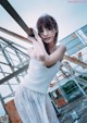 A woman in a white dress leaning against a metal structure.