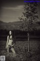 A naked woman standing in a field next to a tree.