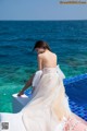 A woman in a white dress sitting on the edge of a swimming pool.