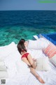 A woman in a red bikini laying on a bed by the ocean.