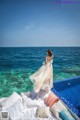 A woman in a long dress standing on the edge of a swimming pool.