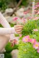 A woman in a white sweater is picking flowers from a bush.