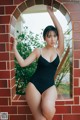 A woman in a black bathing suit leaning against a brick wall.