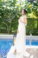 A woman in a white dress standing by a swimming pool.