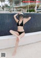 A woman in a black bikini sitting on the edge of a pool.