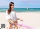 A woman in a white top and floral bikini sitting on a beach.