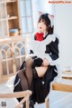 A woman in a maid outfit sitting on a chair.