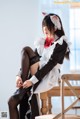 A woman in a maid outfit sitting on a chair.