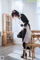 A woman in a maid outfit sitting on a chair.