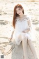 A woman in a white dress sitting on a sandy beach.