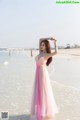 A woman in a pink and yellow dress standing on a beach.