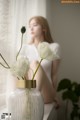 A woman sitting on a window sill next to a vase of flowers.