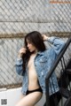 A woman in a denim jacket leaning against a fence.