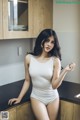 A woman in a white bodysuit posing in a kitchen.