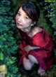 A woman in a red dress crouching down in the woods.