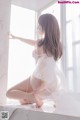 A woman in a white lingerie sitting on a window sill.