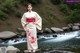 A woman in a kimono standing on a rock by a river.