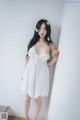 A woman in a white dress leaning against a wall.