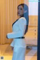 A woman in a white suit standing in front of a glass door.