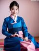 A woman in a blue and pink hanbok sitting on the floor.