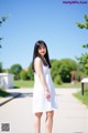 A woman in a white dress standing on a sidewalk.