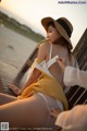 A woman in a yellow dress and hat sitting on a wooden dock.